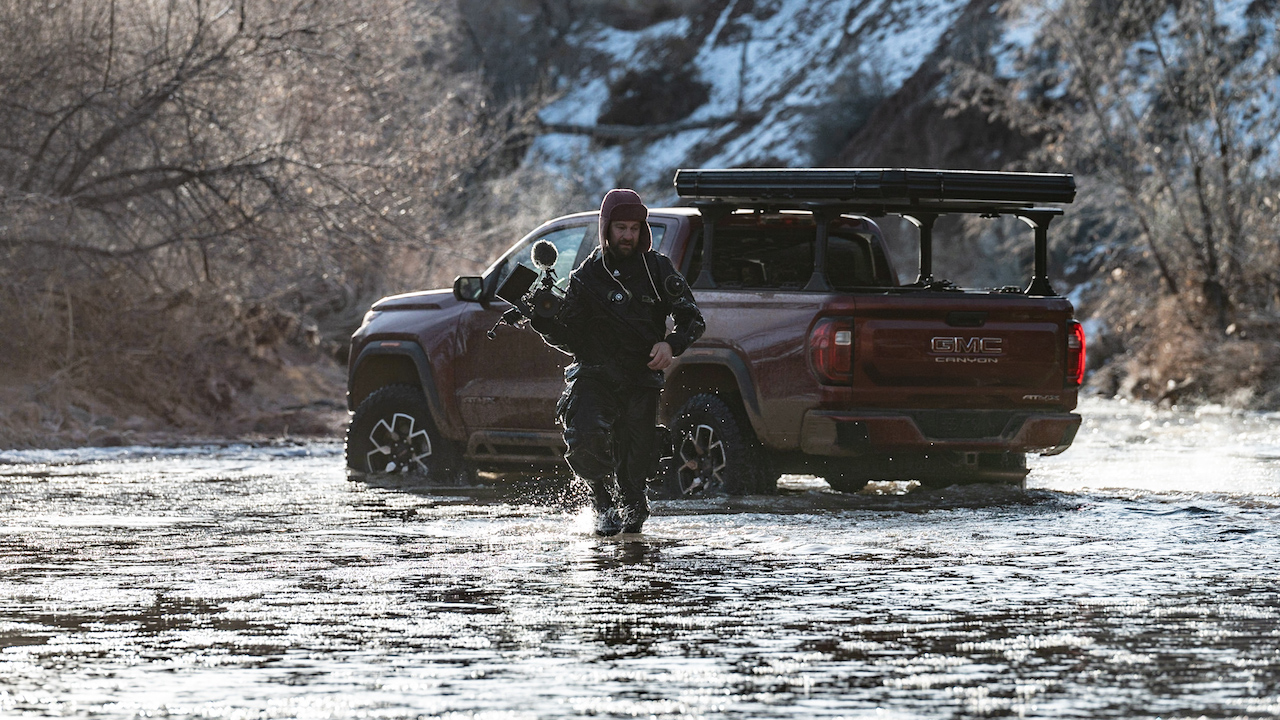 walking through river with RED camera, GMC truck in background
