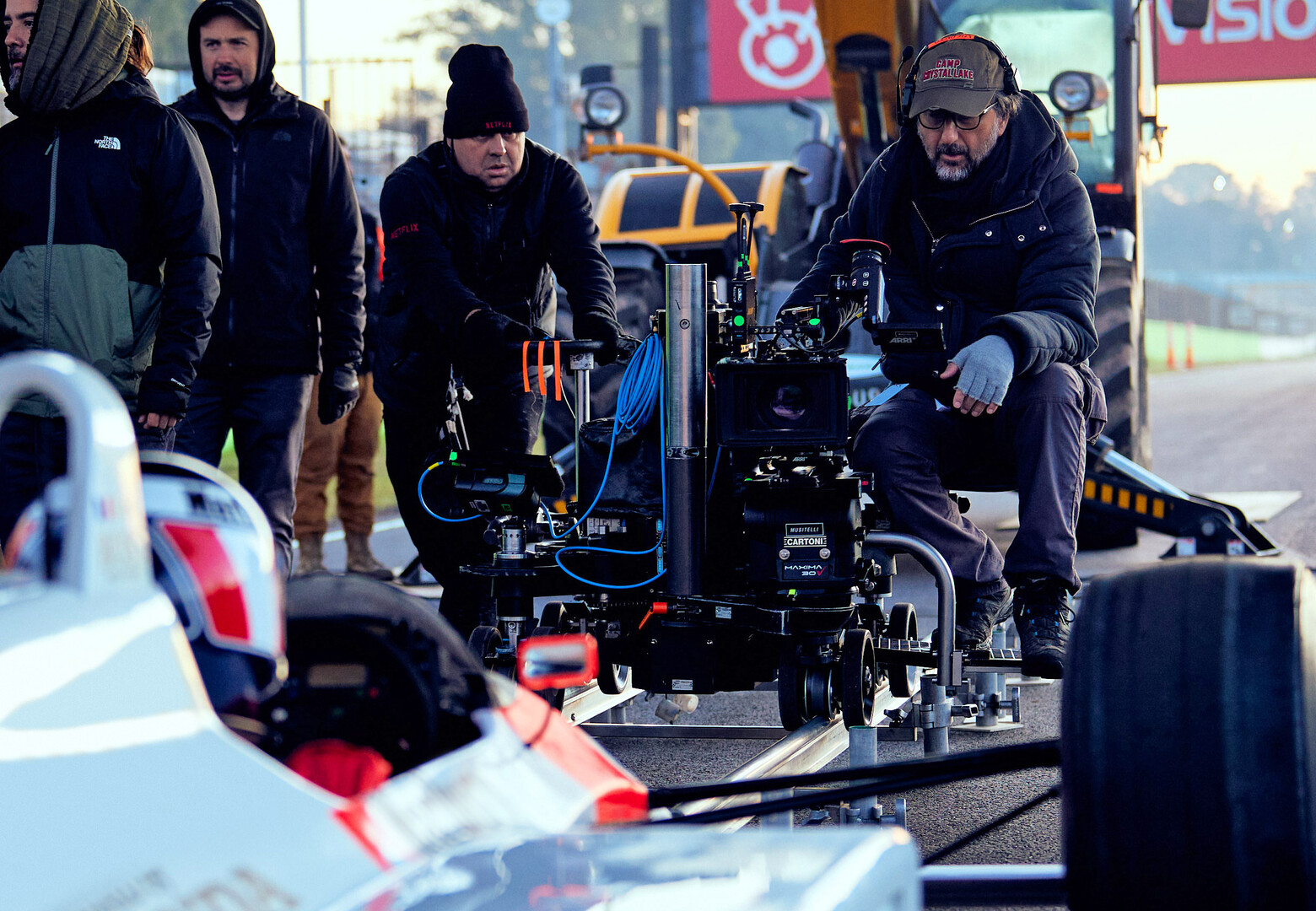 The back of an formula 1 driver in a car with a camera crew in the background