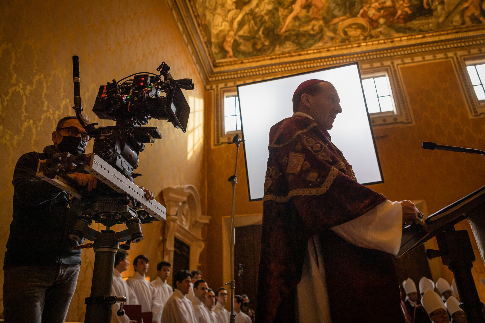 Actor Ralph Fiennes facing right with director of photography Stéphane Fontaine filming him from behind