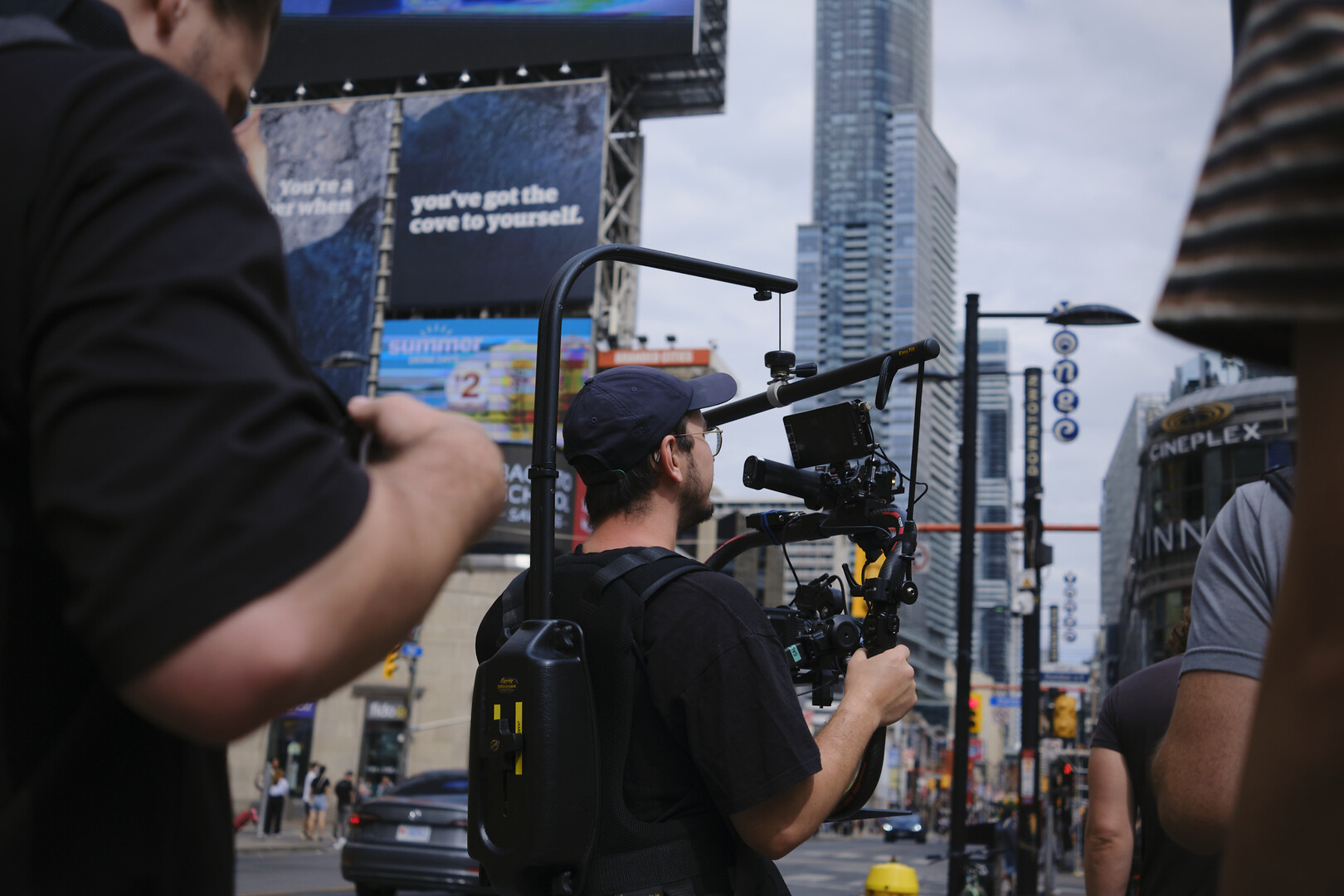 cameraman holding a steadycam rig with a skyscraper in the background