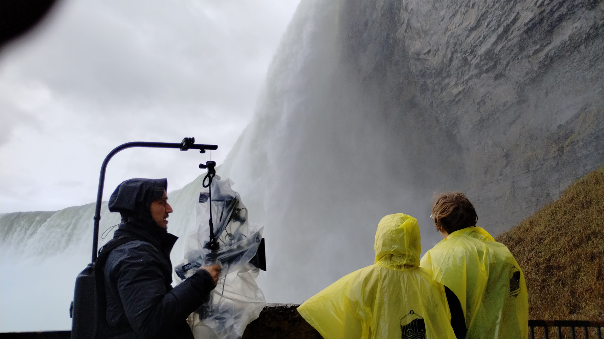 steadycam operator filming two people in raincoats looking at a waterfall
