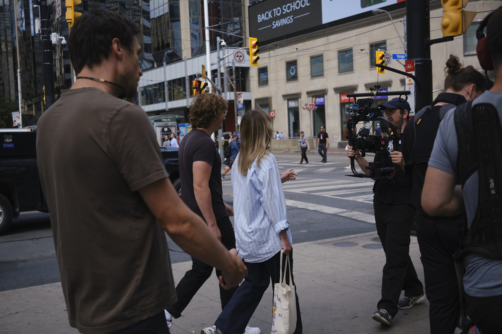 the cast walking on a sidewalk in front of a steadycam rig