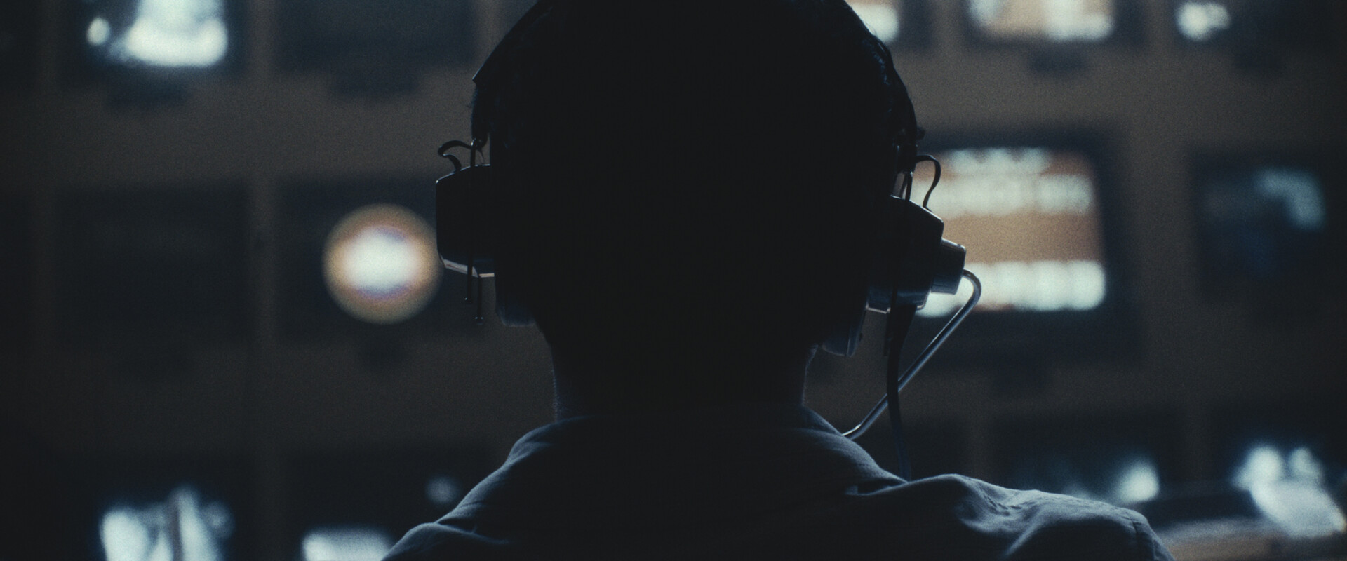 the back of a man's head wearing a headset and looking at monitors