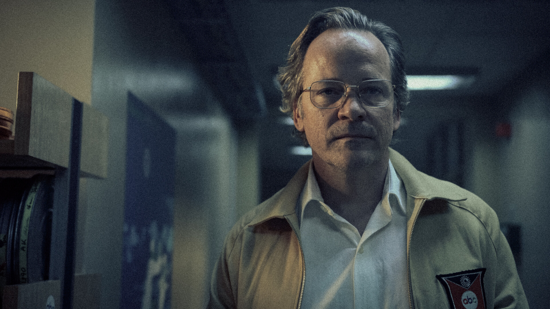 close up of Peter Sarsgaard walking down a hallway wearing glasses