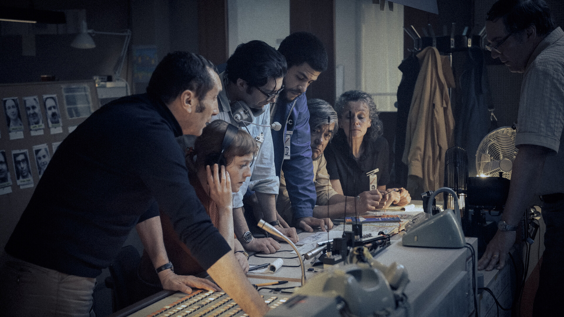 a woman listens intently wearing headphones while others stand around her